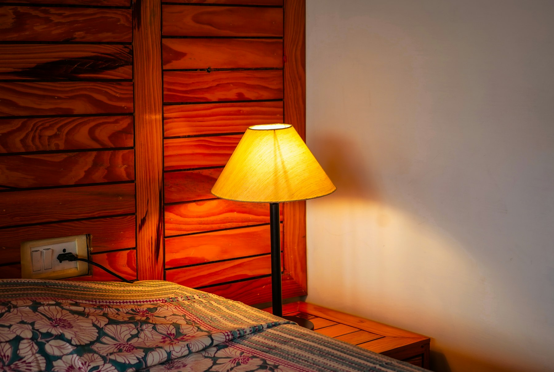 Colț de cameră cu lampă și pat cu cuvertură înflorată