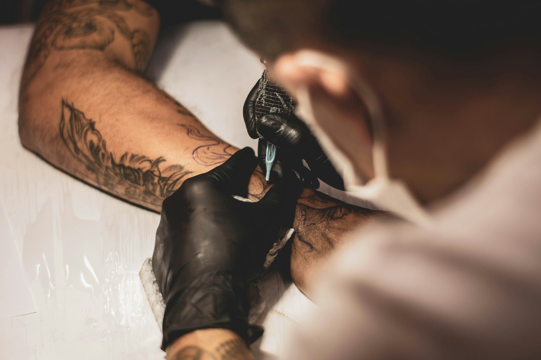 Artist tatuând un braț, în alb-negru